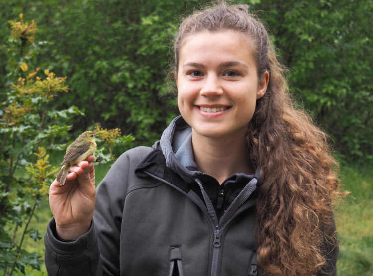 Finola similes at the camera as she holds an orange crowned warbler in her right hand.