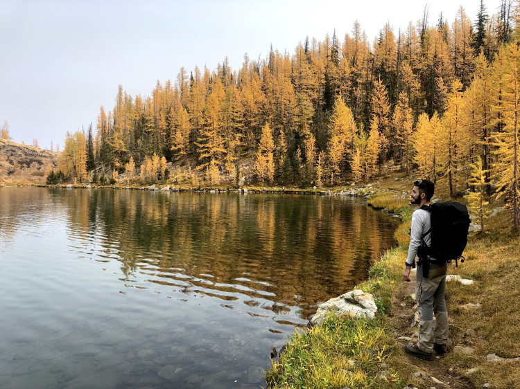 Mitch Fennell stands near the edge of a mountain lake surrounded in fall coloured trees.