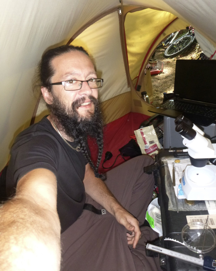 A selfie of Colin in his tent. He is cramped in there with equipment including a computer and microscope.